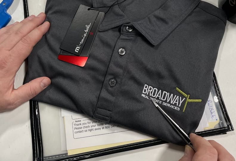 Three custom embroidered red, white, and blue Port Authority polo shirts showing completed business logo embroidery